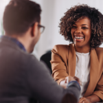 A smiling saleswoman engaging in a handshake with a client across the table, showcasing what the key differences in customer interactions can look like.