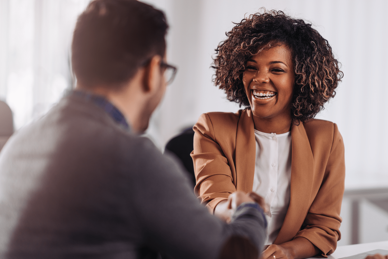 A smiling saleswoman engaging in a handshake with a client across the table, showcasing what the key differences in customer interactions can look like.