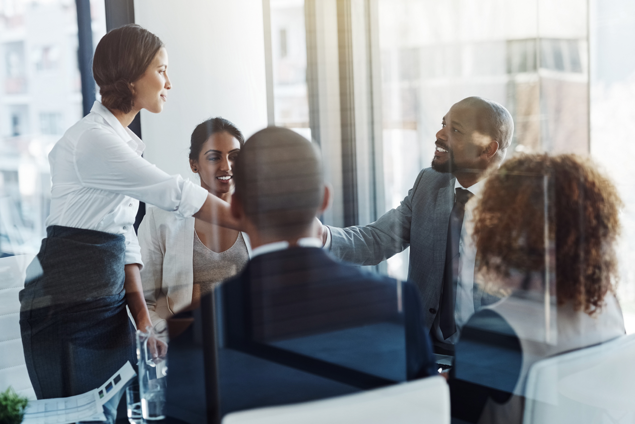 A diverse team of professionals in a collaborative meeting where a saleswoman stands presenting, an example of a sales strategy for alignment and buy-in.