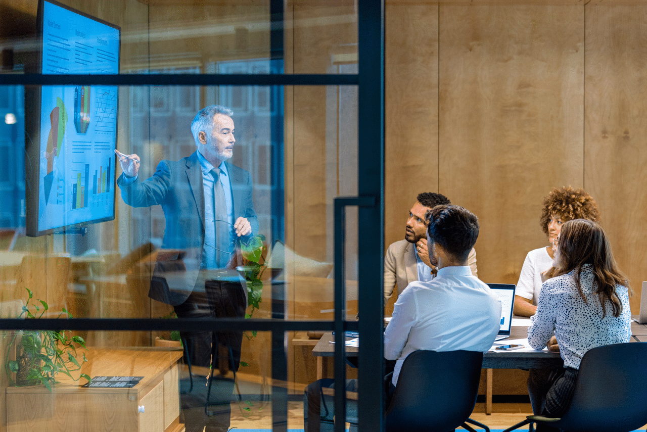 A salesperson delivers a presentation to a group of business people, utilizing effective presentations and marketing materials, as seen on the screen, to communicate key points in an office setting.